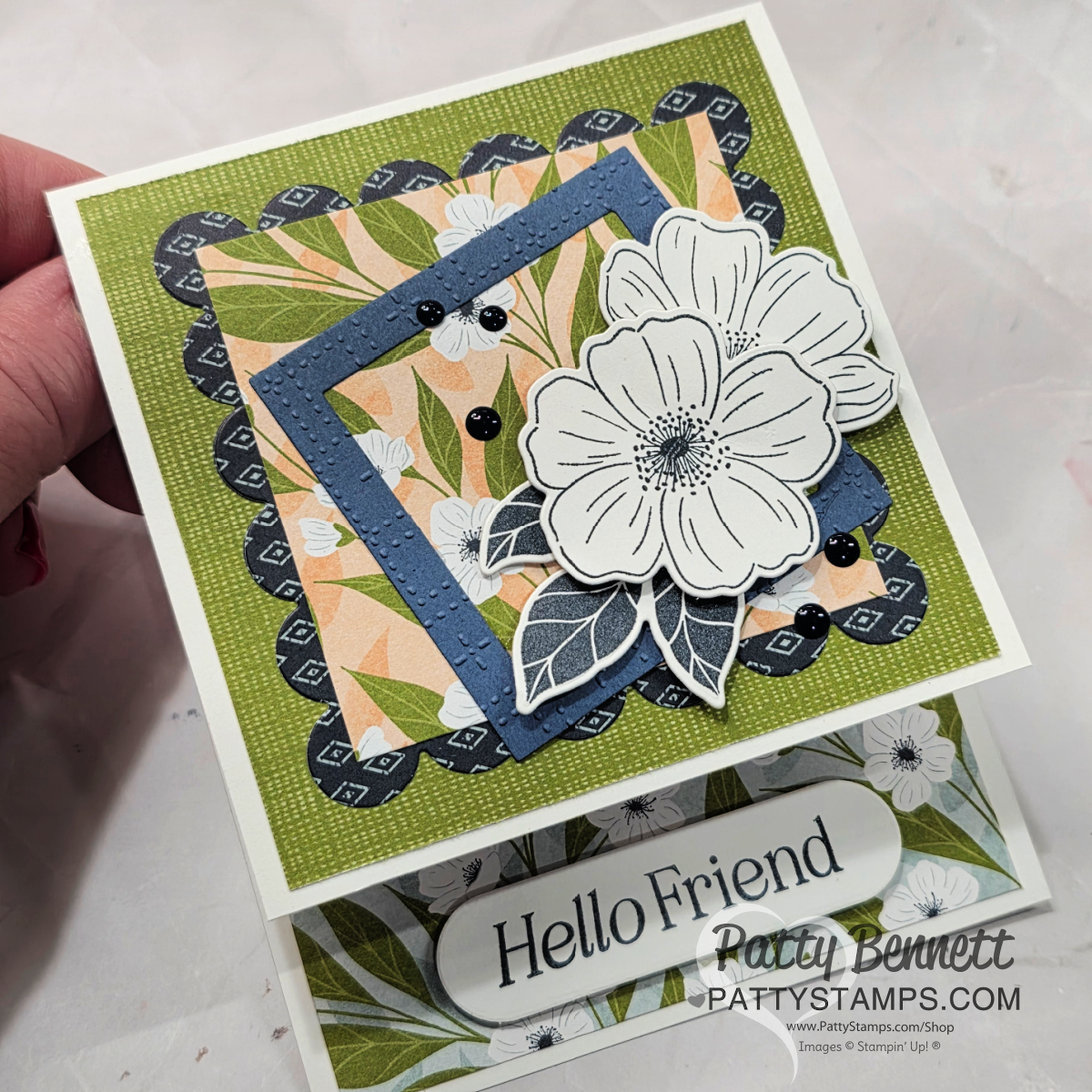 A handmade greeting card features layered, scalloped, and square papers with floral designs in green, blue, and peach. At the center are outlined white flowers with leaves. The card reads "Hello Friend" and is credited to Patty Bennett at pattystamps.com. To read more, visit Patty Stamps (pattystamps.com)