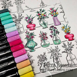A partially colored page shows black-and-white sketches of flower vases. Some vases and flowers are brightly colored with markers in pink, teal, and yellow shades. Several dual-tip markers in similar colors are arranged to the left of the page. To read more, visit Patty Stamps (pattystamps.com)