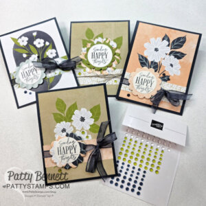 Four handmade greeting cards with floral designs in black, white, and green hues, each decorated with a black ribbon and “Sending Happy Thoughts” sentiment, are displayed alongside a package of colorful adhesive embellishments on a light surface. To read more, visit Patty Stamps (pattystamps.com)