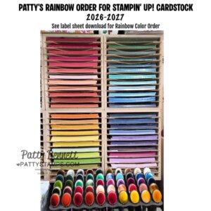 A wooden shelf holds neatly stacked cardstock sheets in a rainbow color order, with reds, oranges, yellows, greens, blues, and purples from top to bottom. Colorful ink blending tools are arranged in two rows below the shelves. Text appears above the shelf. To read more, visit Patty Stamps (pattystamps.com)