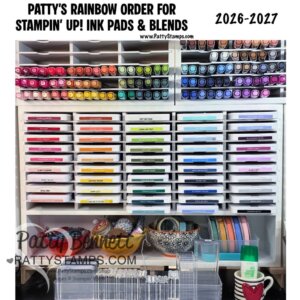 A white shelving unit organizes Stampin’ Up! ink pads, markers, and blends by rainbow color. Bowls hold small tools and rolls of tape sit below. The header reads “PATTY’S RAINBOW ORDER FOR STAMPIN’ UP! INK PADS & BLENDS 2026–2017.” Website and watermark included. To read more, visit Patty Stamps (pattystamps.com)