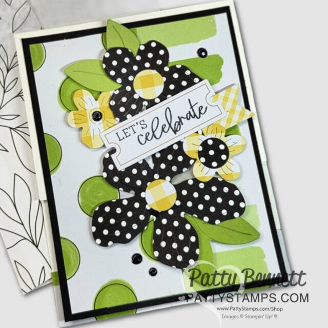 Quick & Easy Card ideas with Ephemera. A handmade card featuring layered black-and-white polka dot flowers with yellow and green centers, green leaves, and a white label in the center that says “LET’S celebrate.” The background is light gray with green circles. The card is signed “Patty Bennett.”. To read more, visit Patty Stamps (pattystamps.com)