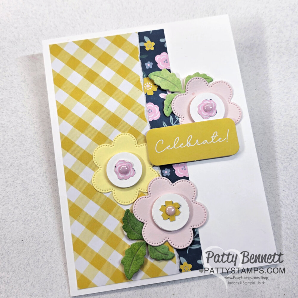 A handmade card with layered paper flowers, yellow checkered and dark floral strips on white cardstock. “Celebrate!” is written on a yellow label, and “Patty Bennett PattyStamps.com” is printed at the bottom right corner. To read more, visit Patty Stamps (pattystamps.com)