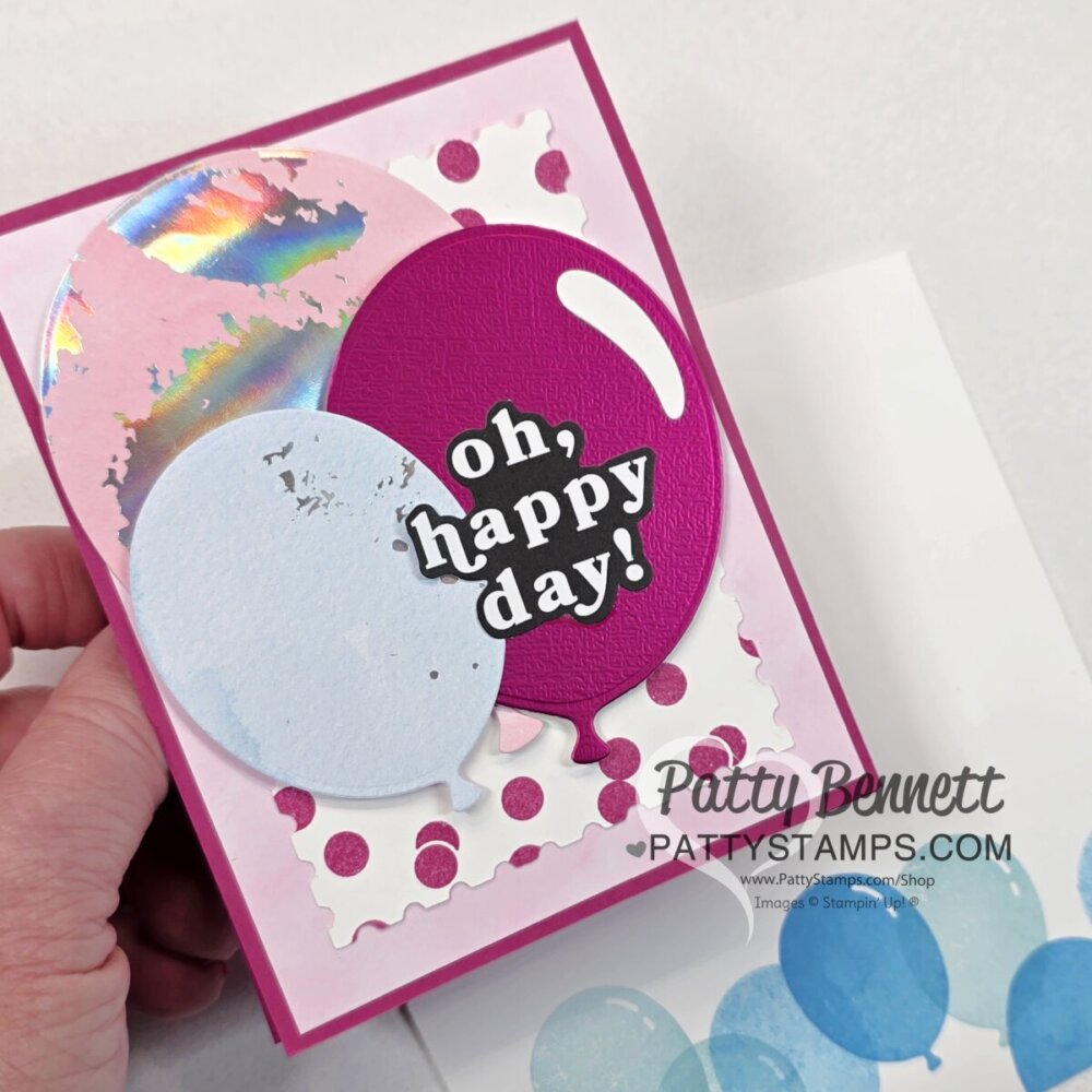 A hand holds a colorful greeting card with large pink and blue balloons, a shiny iridescent circle, and a white jagged frame. The card features the bold text “oh, happy day!” on a purple balloon. Below is the watermark: PattyBennett.com PattyStamps. To read more, visit Patty Stamps (pattystamps.com)