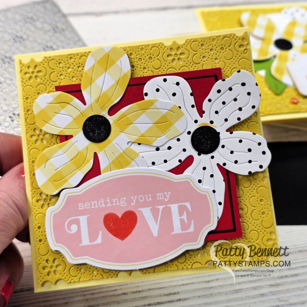 A handmade card with a textured yellow background features two large flowers—one yellow plaid, one white with black dots—and a red panel. At the bottom, a pink label reads “sending you my LOVE” with a red heart replacing the "O". To read more, visit Patty Stamps (pattystamps.com)
