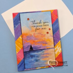 A handmade card features a painted sunset over water with a small sailboat, and the words “Thank you for being there for me.” The border has a diagonal geometric pattern in rainbow colors. The envelope is white and the card is signed "Patty Bennett. To read more, visit Patty Stamps (pattystamps.com)