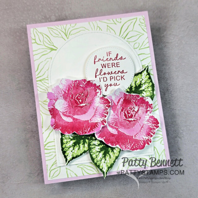 Handmade card with two pink and white roses, green leaves, and a textured white background with leaf patterns. A circular sentiment reads, “If friends were flowers I’d pick you” in pink script. Card is signed Patty Bennett, with a watermark at the bottom right. To read more, visit Patty Stamps (pattystamps.com)