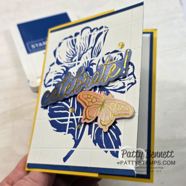 A handmade card with a large blue floral design, gold and blue "celebrate!" text, and a pink and gold butterfly embellishment. The card is layered on yellow and blue cardstock. "Patty Bennett PattyStamps.com" is watermarked on the image. To read more, visit Patty Stamps (pattystamps.com)