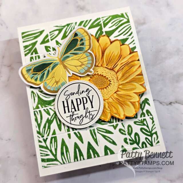 Handmade card with green leafy background, large yellow sunflower, blue-yellow butterfly, and round tag reading “Sending HAPPY thoughts.” Card is angled on a marble surface. “Patty Bennett” and her website watermark appear in the bottom right corner. To read more, visit Patty Stamps (pattystamps.com)