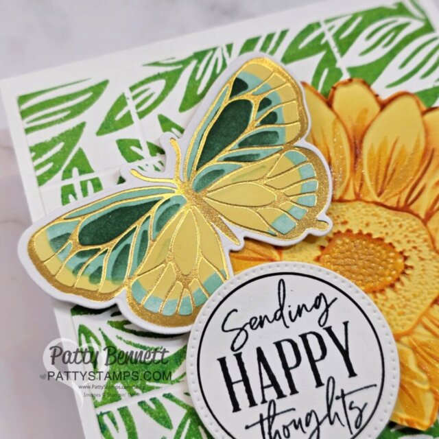 A handmade greeting card features a yellow and teal butterfly with gold accents, a large yellow sunflower, green leafy background, and a circular sentiment that reads "Sending HAPPY thoughts." The card has intricate textures and vibrant colors. To read more, visit Patty Stamps (pattystamps.com)