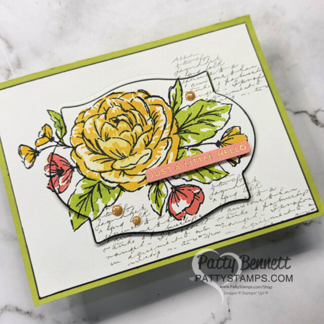 A handmade greeting card with a large yellow flower, red buds, and green leaves on a white, ornate label. Handwritten script decorates the background. A small strip reads “Just a Little Hello.” Card edges are green. The PattyStamps.com logo appears in the bottom right. To read more, visit Patty Stamps (pattystamps.com)