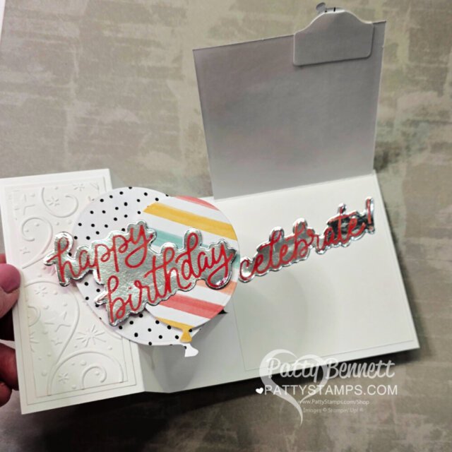 A hand holds an open pop-up birthday card with a colorful striped and polka dot circle. Shiny red text reads "happy birthday celebrate!" Floral embossed designs decorate the card. A watermark says Patty Bennett PattyStamps.com. To read more, visit Patty Stamps (pattystamps.com)