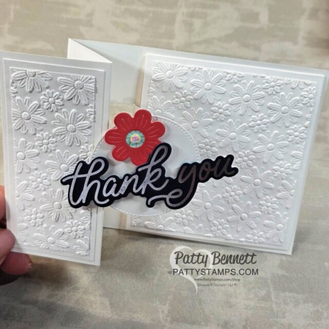 A handmade white greeting card embossed with daisy patterns features a red flower and a bold black script "thank you" on the front. The card is displayed partially open on a beige surface, with "Patty Bennett PATTYSTAMPS.COM" printed below. To read more, visit Patty Stamps (pattystamps.com)