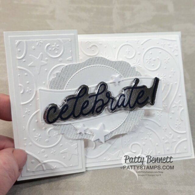 A hand holds a white embossed greeting card with swirling patterns and stars. The front flap features a layered scalloped circle, silver accents, and a shiny black script that reads “celebrate!” Small white stars decorate the center design. To read more, visit Patty Stamps (pattystamps.com)